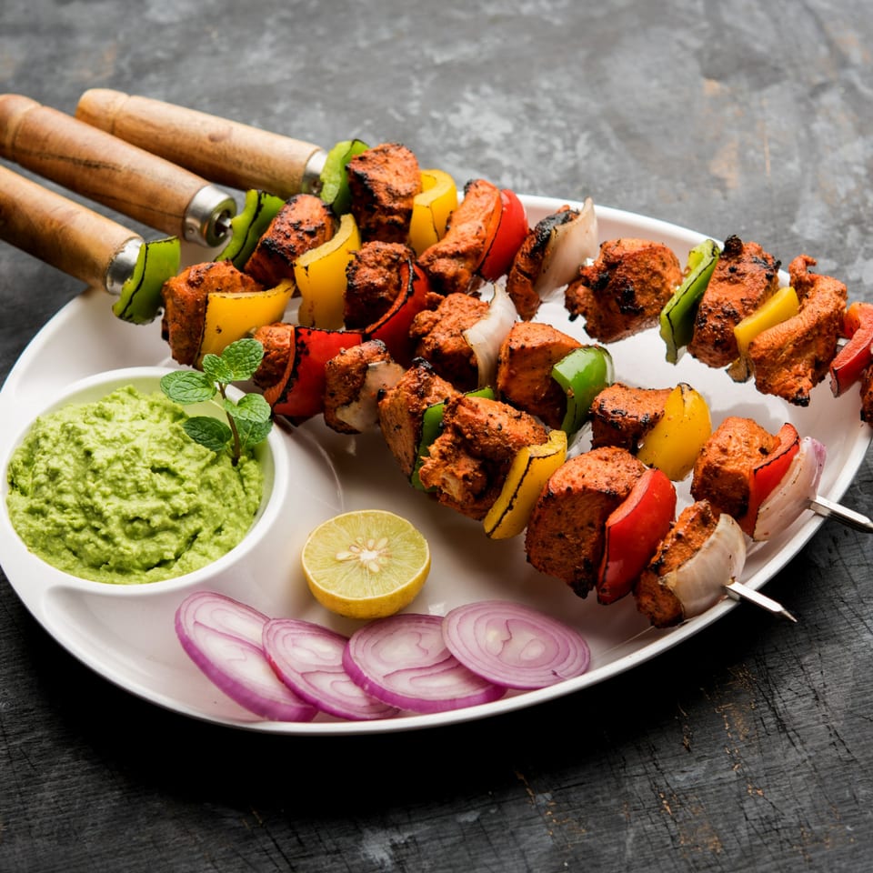 Chicken tikka skewers with bell peppers and onions, served with green chutney, lime, and red onion.