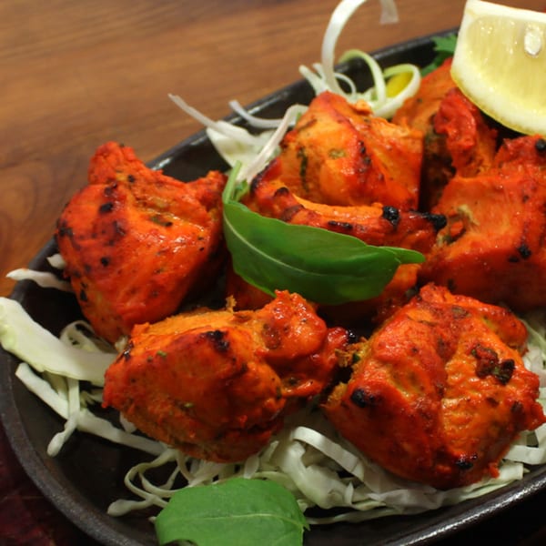 Bright orange Indian chicken tikka pieces, garnished with shredded cabbage, a green leaf, and a lemon wedge.