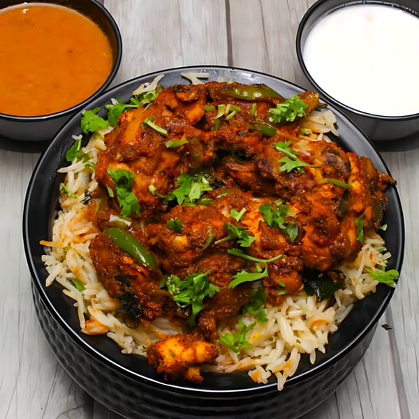 Chicken Biryani with green peppers and cilantro, served with a side of curry and raita.