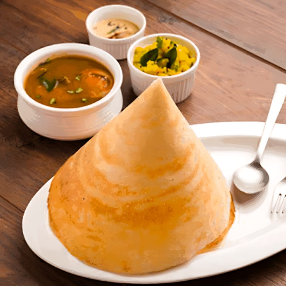 A cone-shaped dosa on a white plate with sambar, chutney, and potato curry.